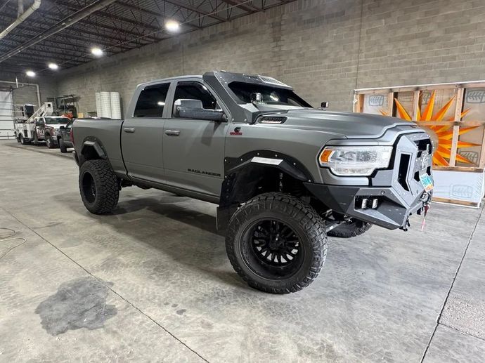 Gray lifted pickup truck with black wheels parked indoors in a warehouse.