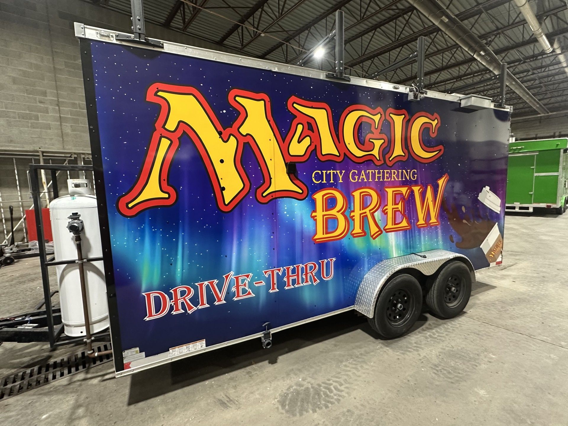 Magic Brew food trailer with purple/orange graphics and “Drive-Thru” text in an indoor warehouse.