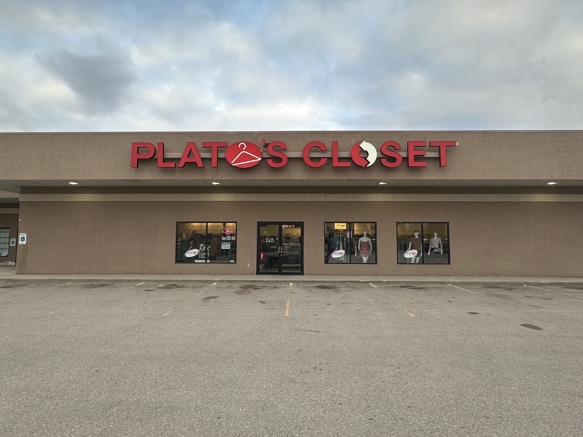 Plato’s Closet storefront with red sign on a beige strip mall facade under a cloudy sky