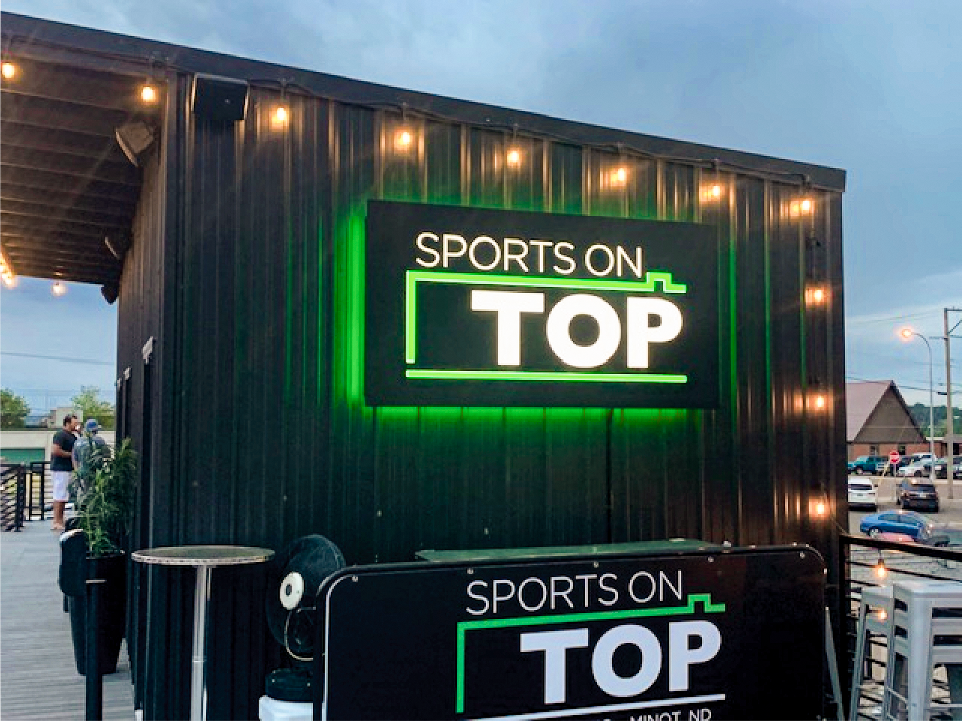 Sports on Top neon sign on a dark wooden building at dusk, with a matching sign in front.