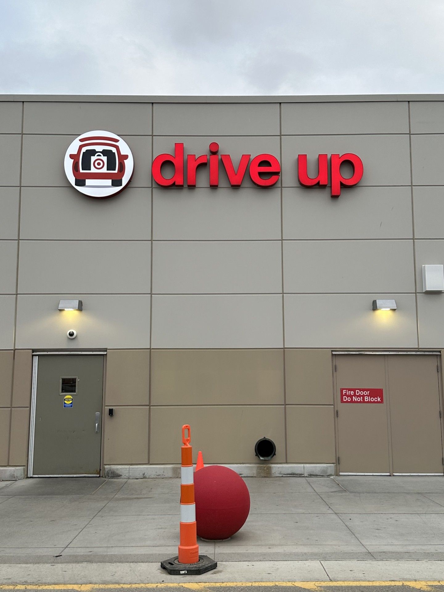 Drive Up storefront with red sign, gray wall, orange cone, and red bollard at the entrance