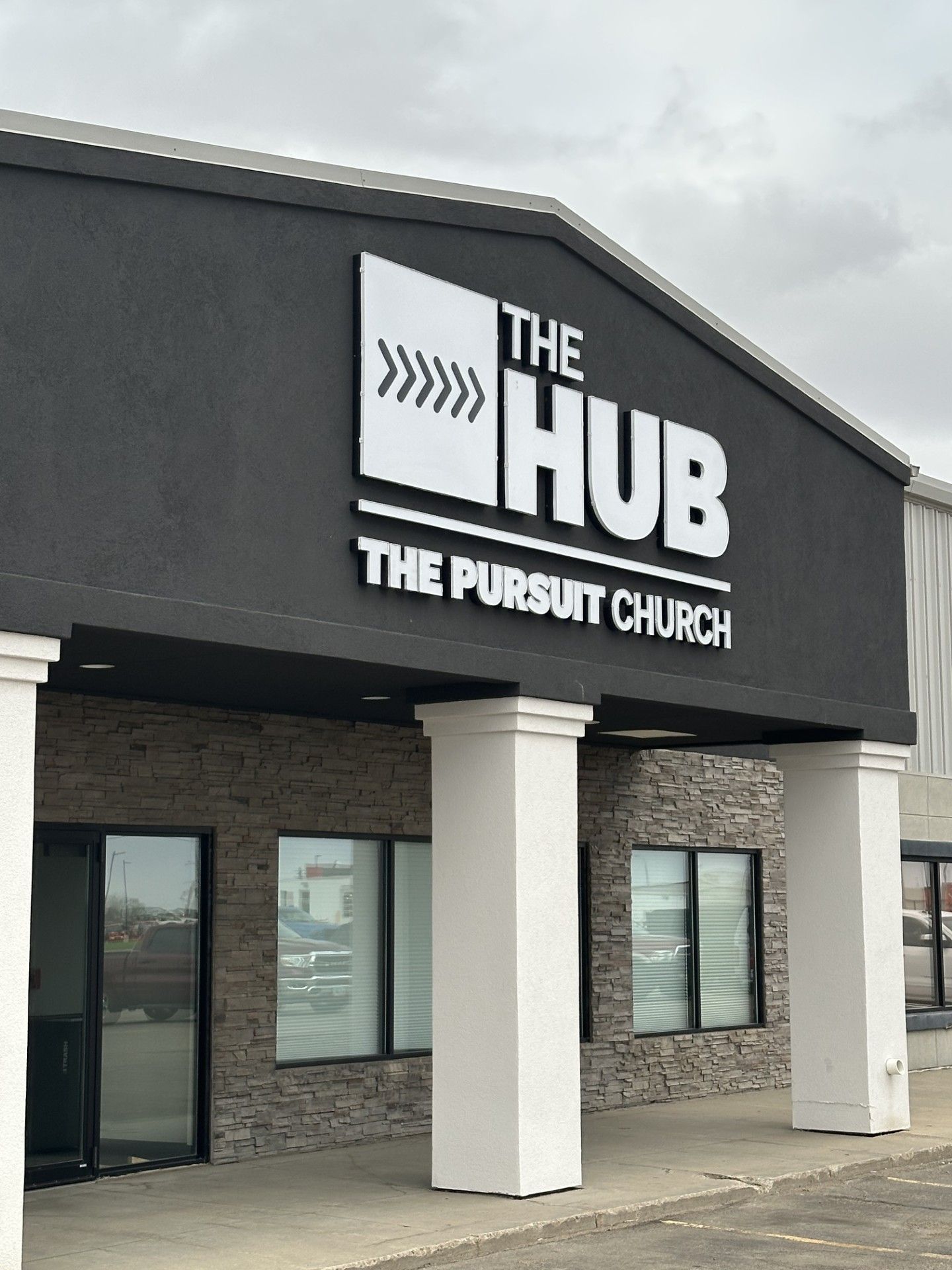 The HUB and The Pursuit Church sign on a dark gray building with white columns