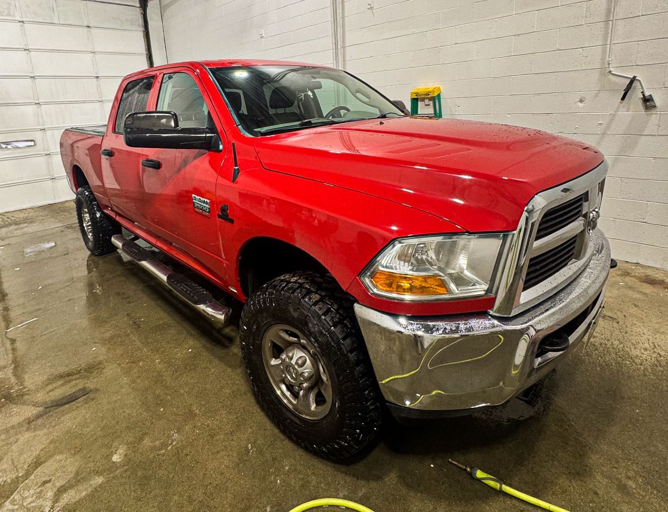Red pickup truck in a wet indoor wash bay, angled front-left view.