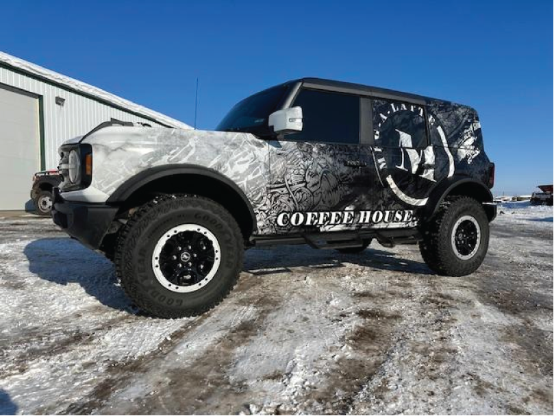 Black-and-white off-road Jeep parked on snowy ground near a building under a clear blue sky