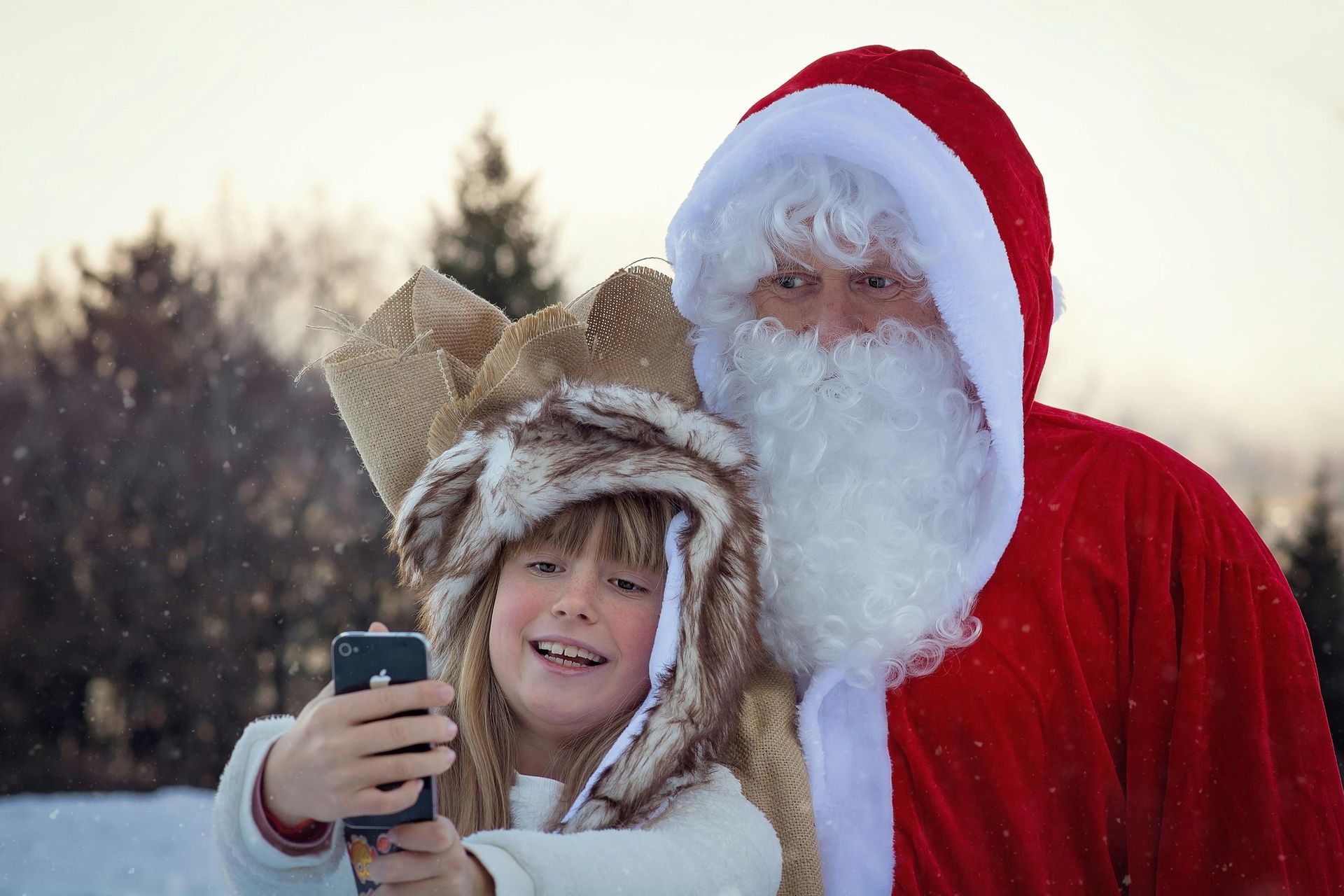A little girl is taking a selfie with santa claus.