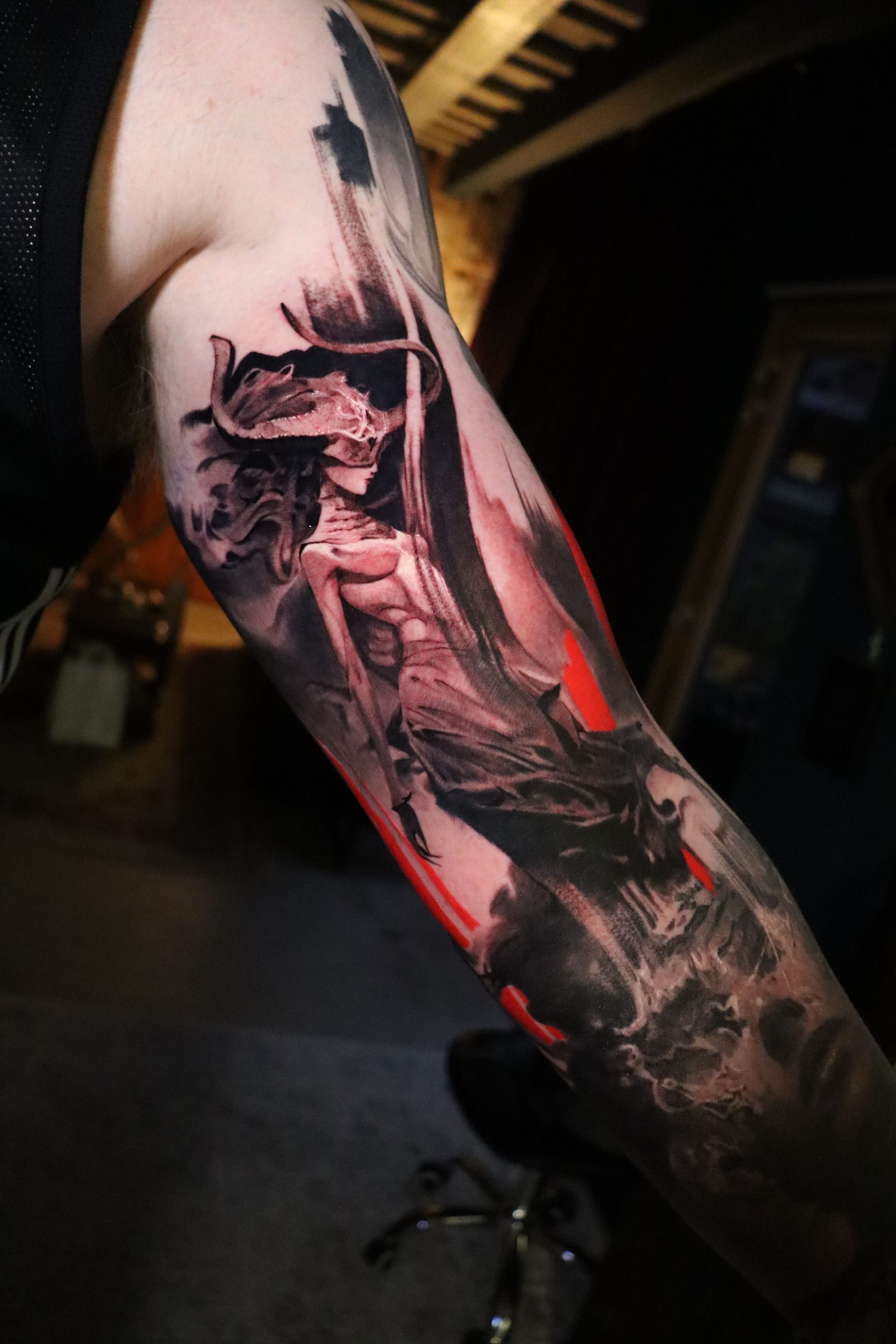 A detailed, dark, illustrative tattoo on an arm featuring a skeletal, horned figure with flowing hair and red accents.