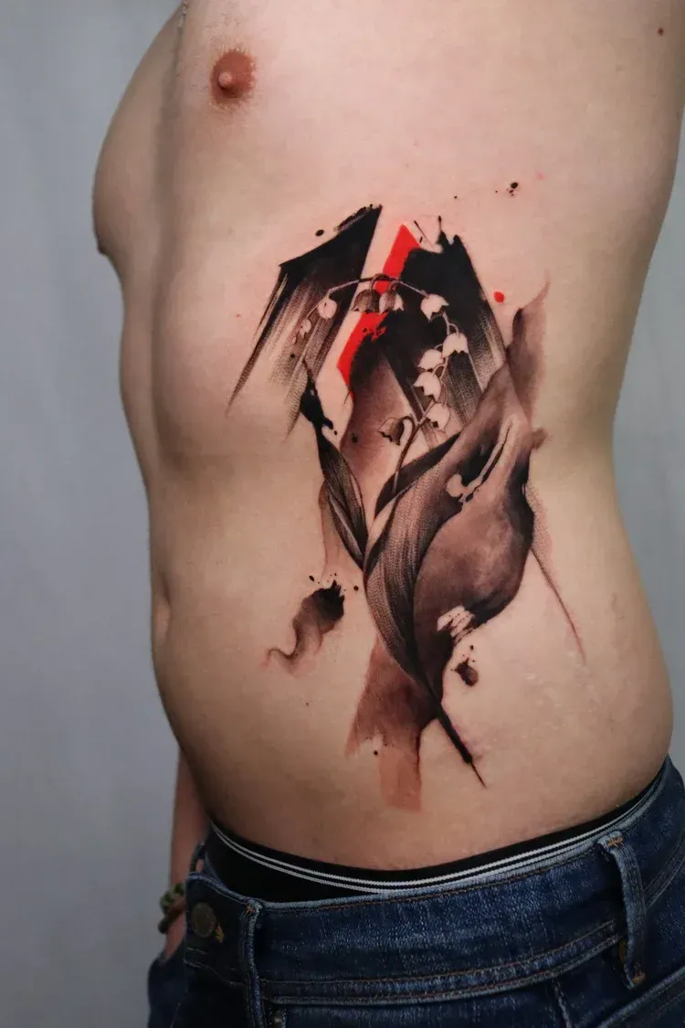 A side-profile view of a torso featuring a black and grey ink tattoo of lilies with bold, abstract red brushstroke accents.