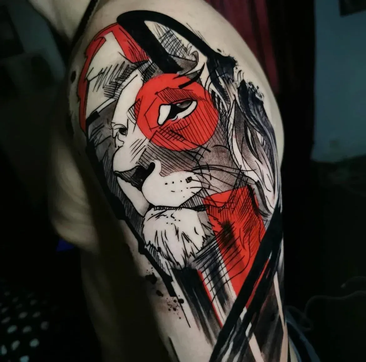 Abstract shoulder tattoo featuring a lion's face in black ink with striking red geometric accents and sketch-like lines.