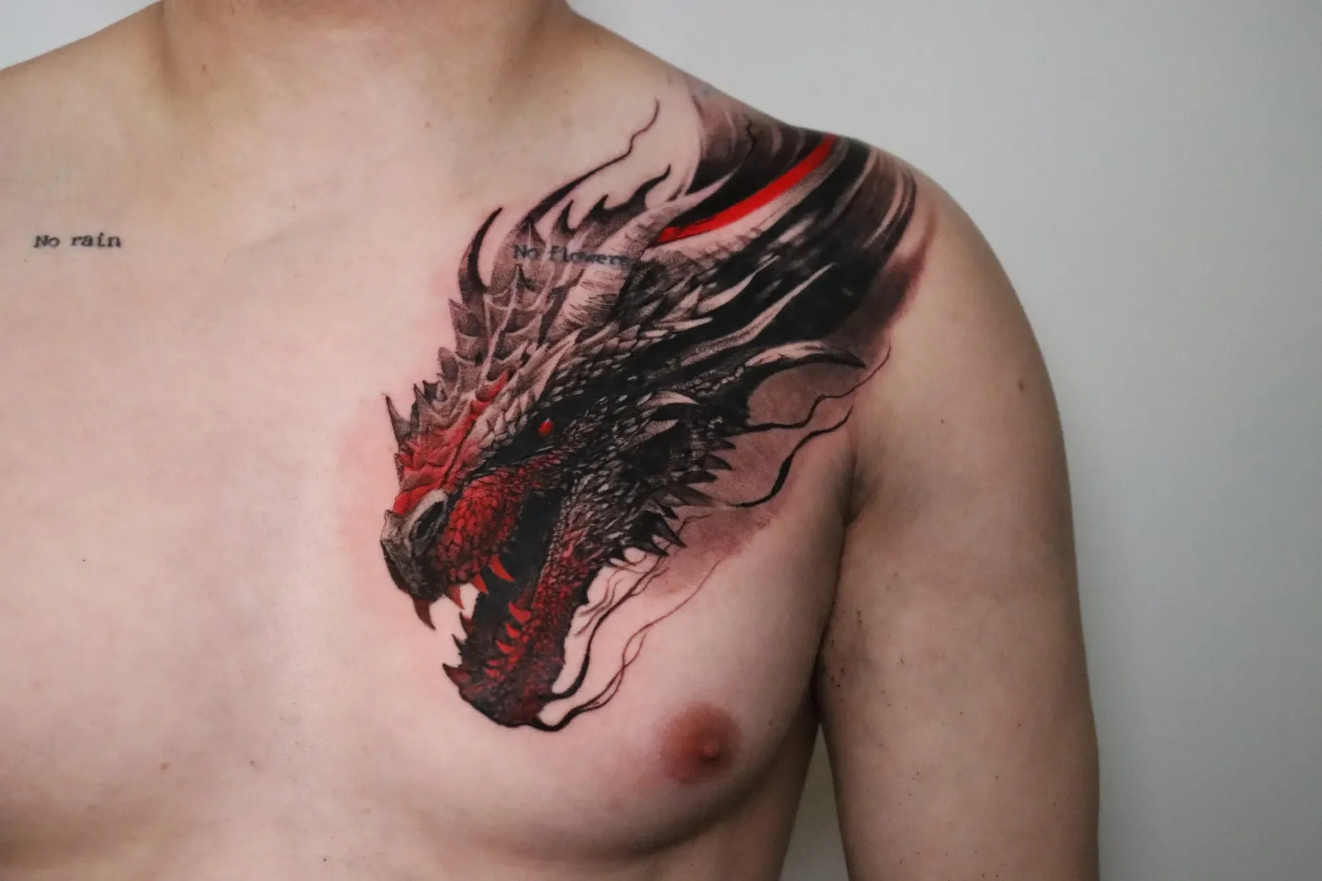 A detailed black and red tattoo of a dragon head positioned on a person's upper chest and shoulder.