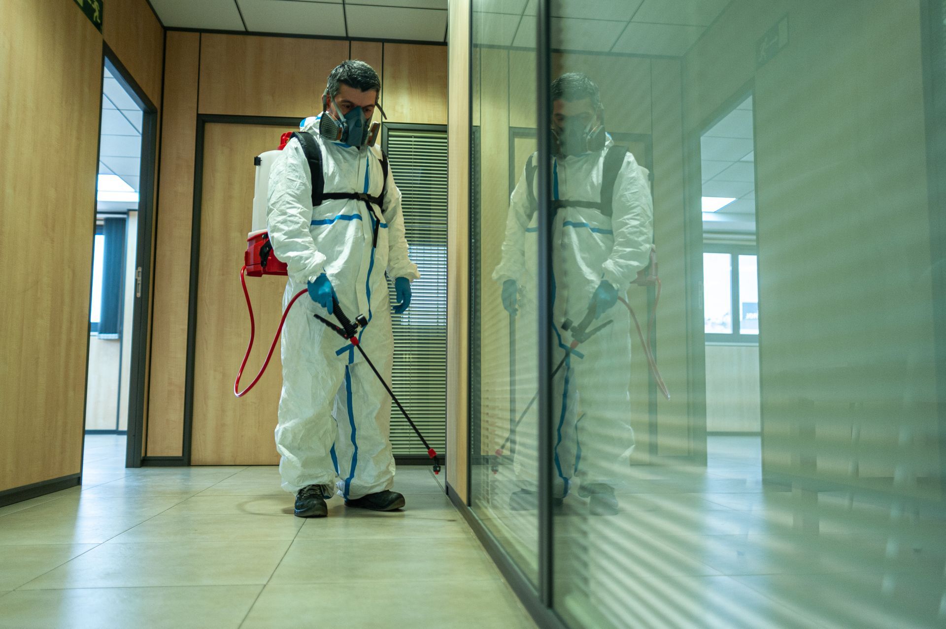 A man in a protective suit is spraying a room with a sprayer.