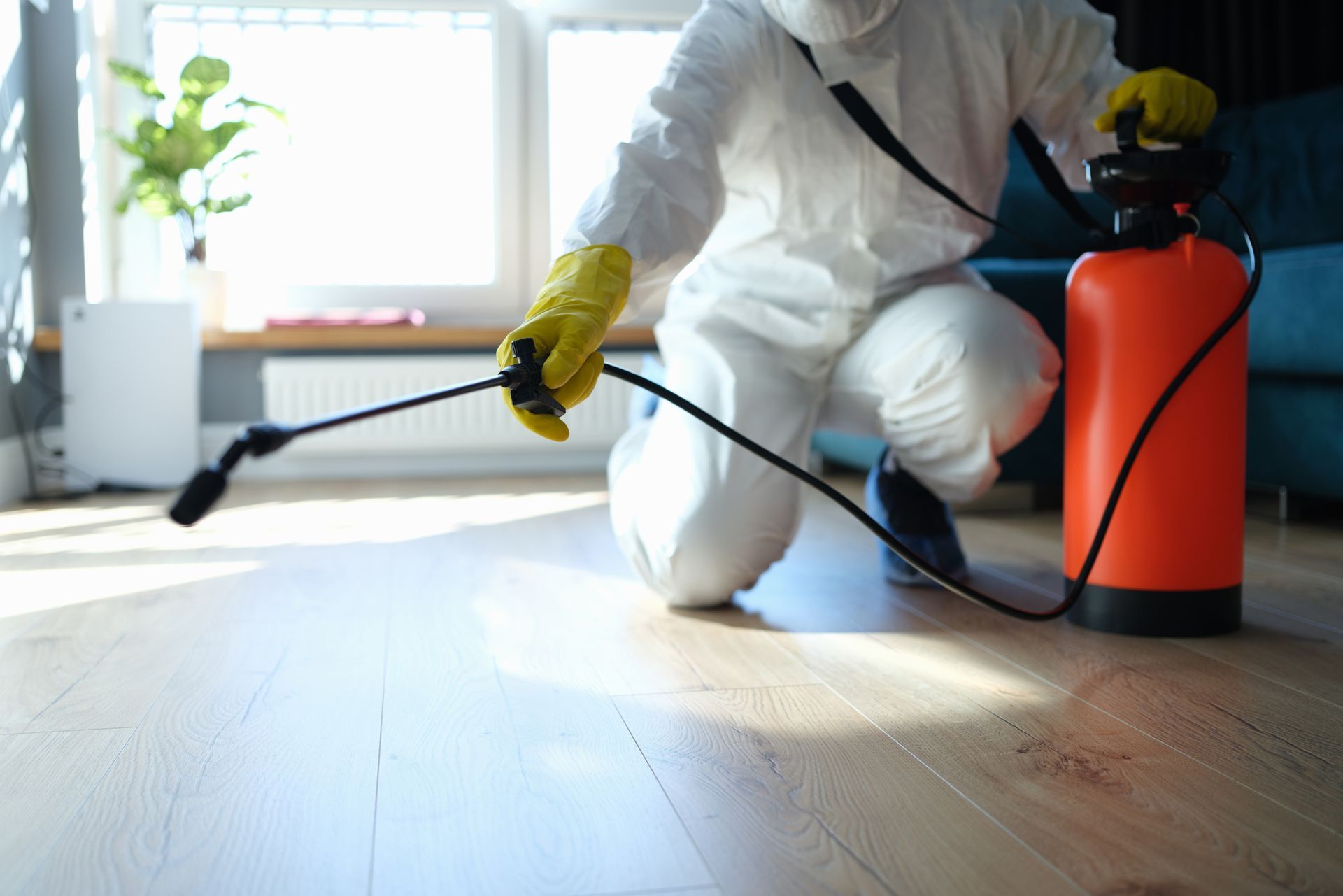 A man in a protective suit is spraying a room with a sprayer.
