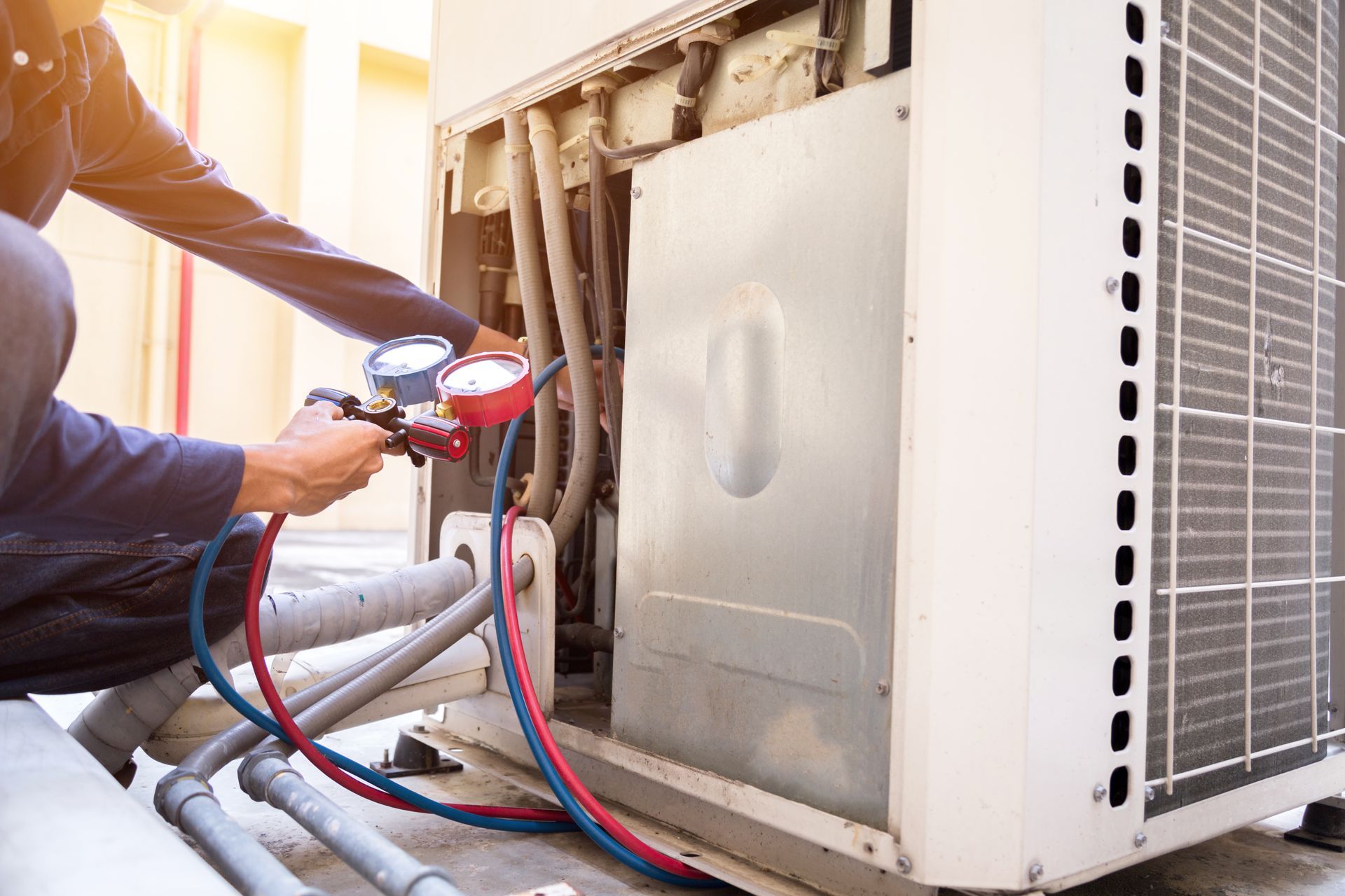 HVAC technician using gauges to service an air conditioning unit outdoors.