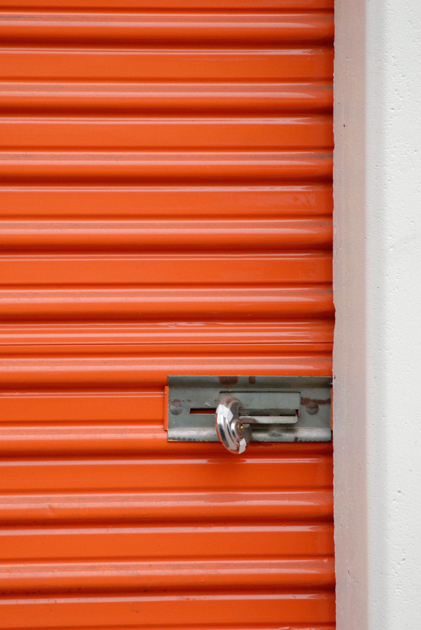 Orange storage unit door with a locked metal latch, next to a white wall.