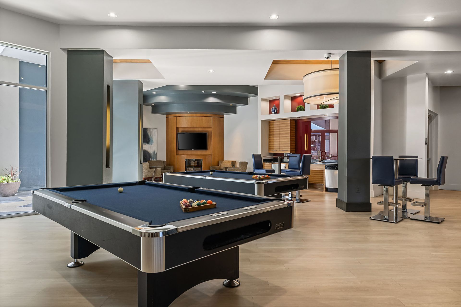 Modern game room with a blue pool table, bar seating, and a TV in the background at The Marq at Ridgegate in Lone Tree, CO.