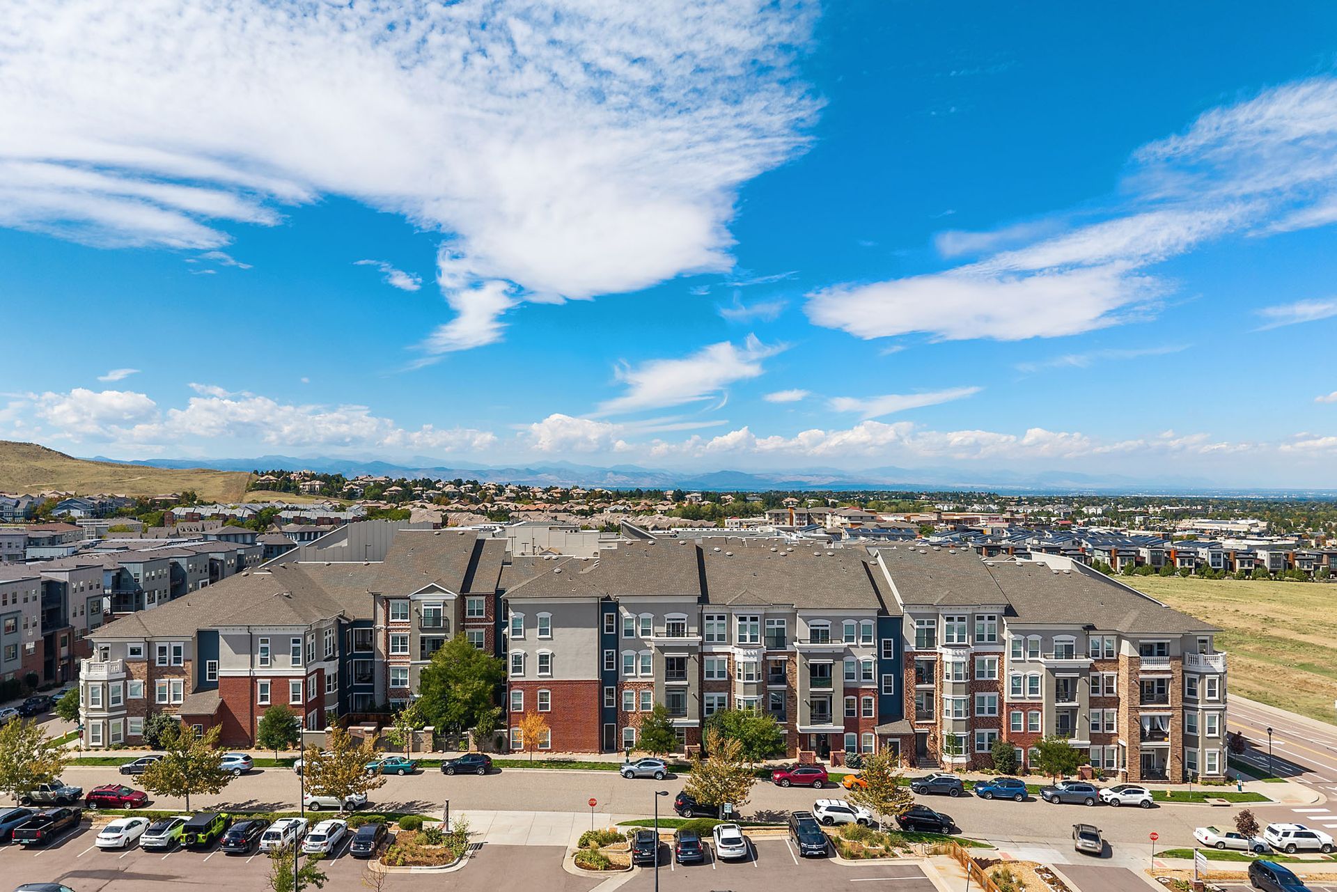 Aerial view of a modern apartment complex with parking lot under a bright blue sky at The Marq at Ridgegate in Lone Tree, CO.