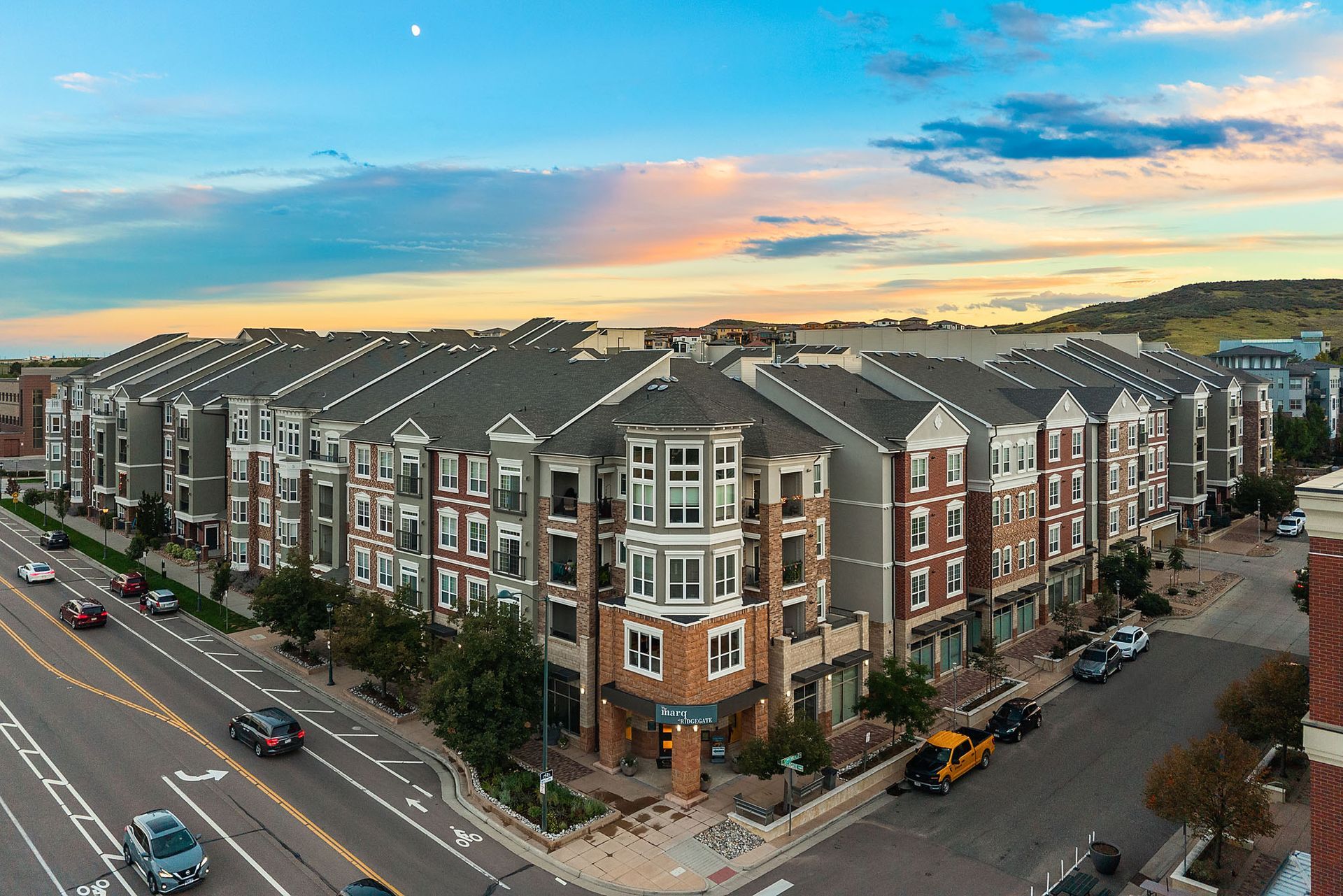 Aerial view of a modern apartment complex at sunset along a city street at The Marq at Ridgegate in Lone Tree, CO.