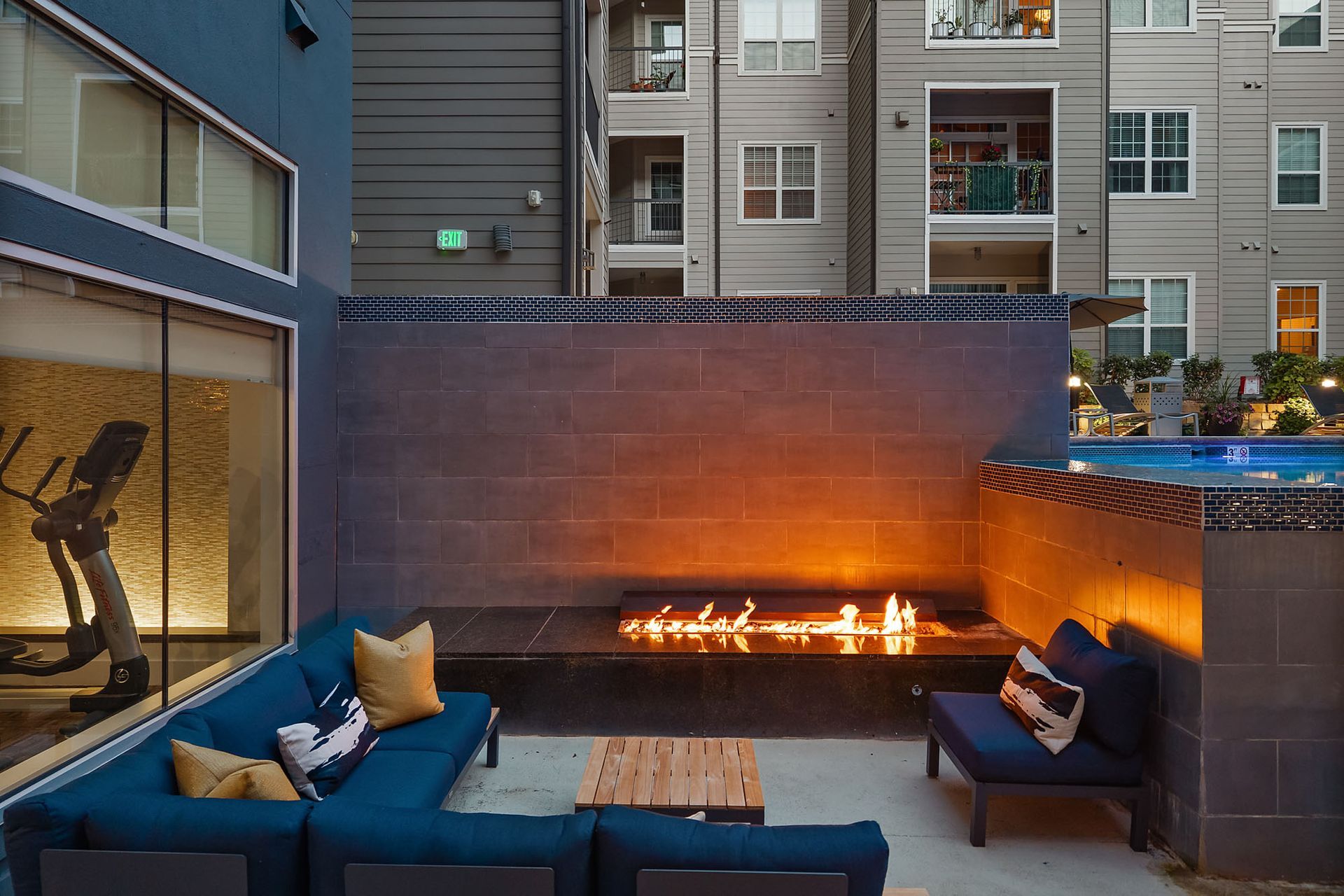 Modern apartment courtyard with blue seating, a fire pit, and tall buildings at dusk at The Marq at Ridgegate in Lone Tree, CO.