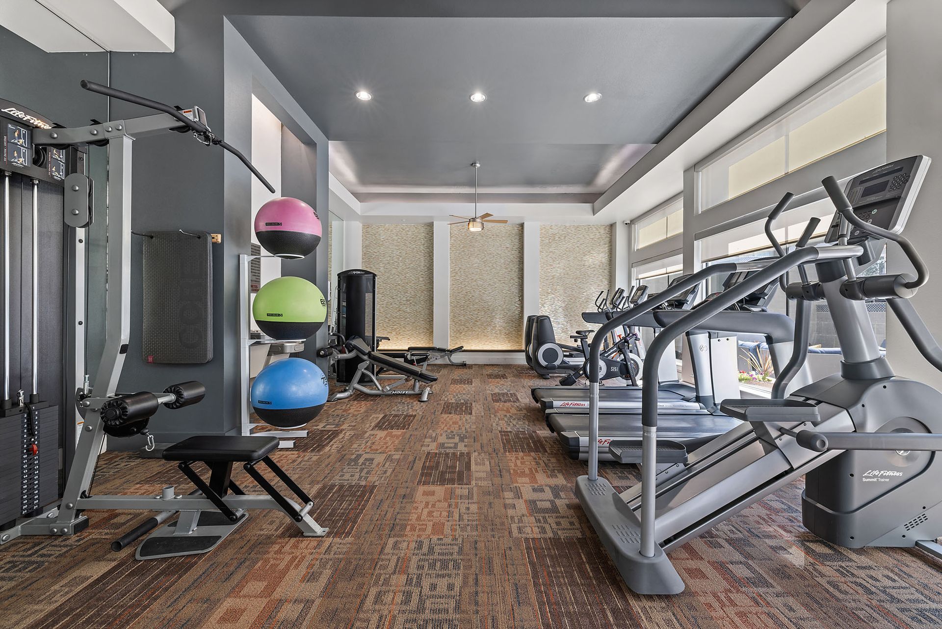 Empty modern gym with treadmills, cable machine, weights, and exercise balls on a patterned floor at The Marq at Ridgegate in Lone Tree, CO.