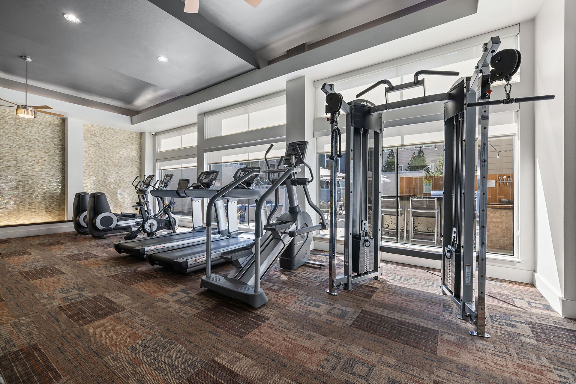 Modern gym room with treadmills, cable machine, and mirrors on hardwood floors at The Marq at Ridgegate in Lone Tree, CO.