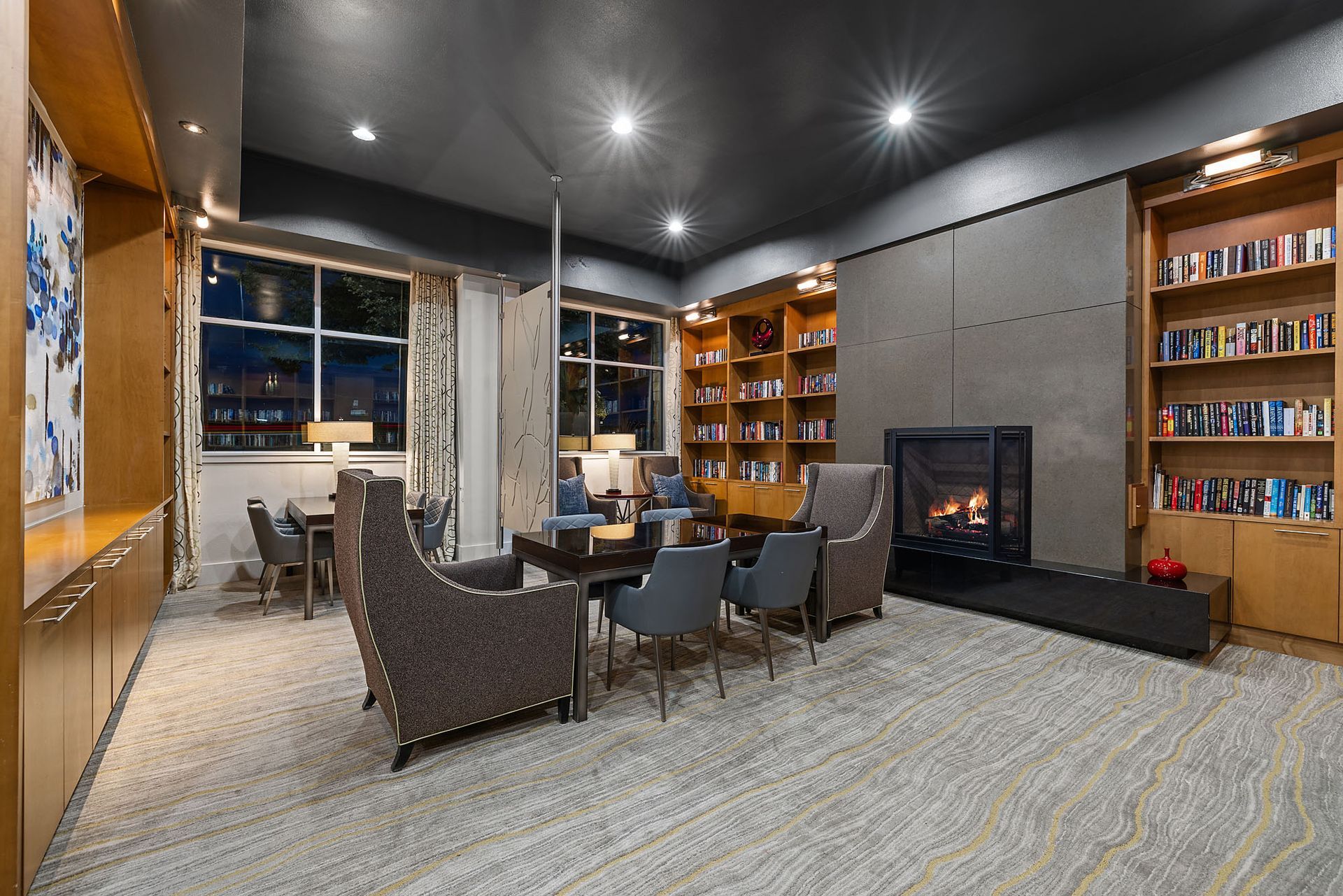 Modern lounge with wicker chairs, tables, bookshelves, and a fireplace under recessed lighting at The Marq at Ridgegate in Lone Tree, CO.
