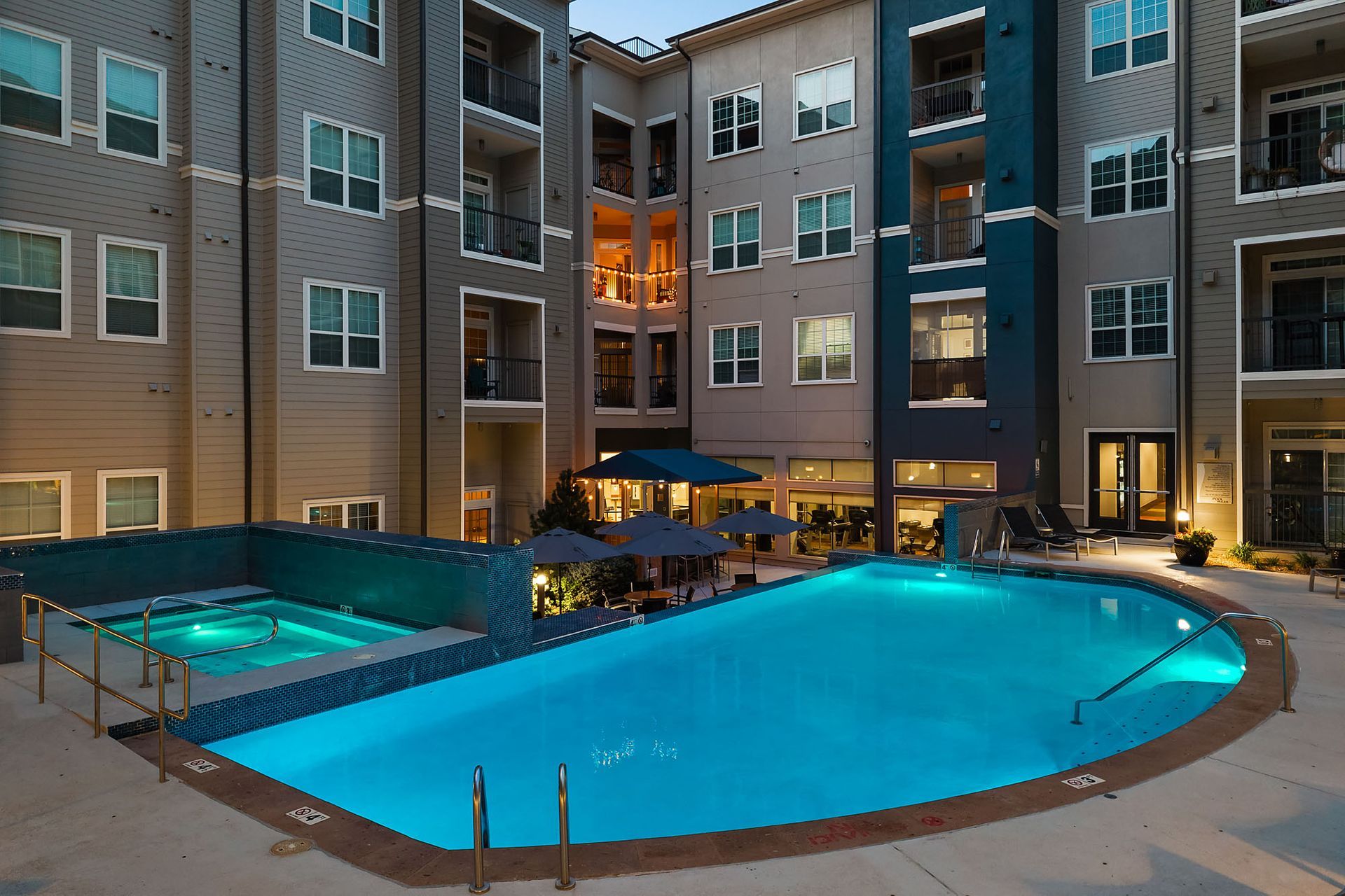 Courtyard apartment pool lit blue at dusk, surrounded by multi-story buildings and lounge seating at The Marq at Ridgegate in Lone Tree, CO.