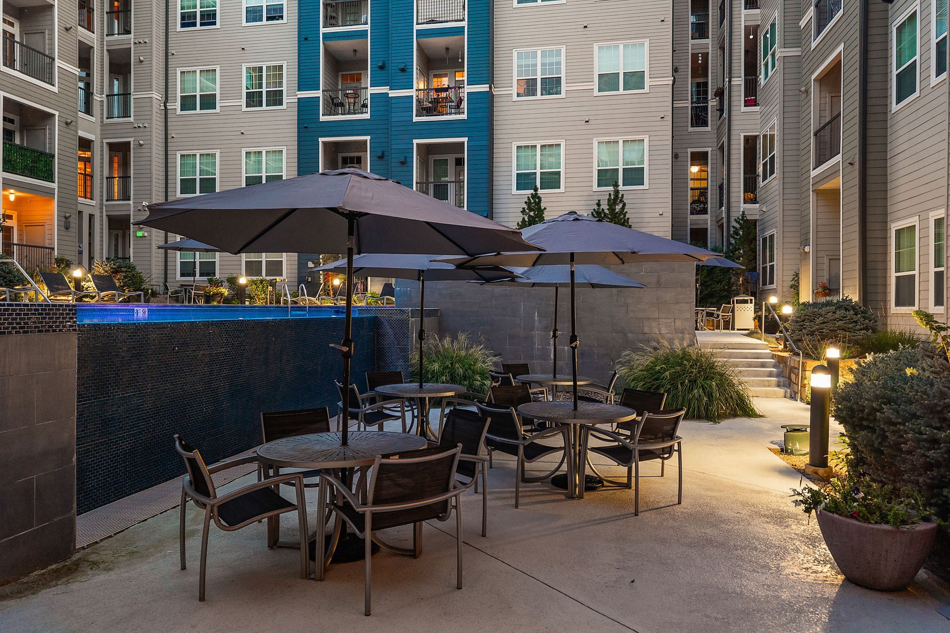 Apartment courtyard patio with tables, umbrellas, and warm lights at dusk at The Marq at Ridgegate in Lone Tree, CO.