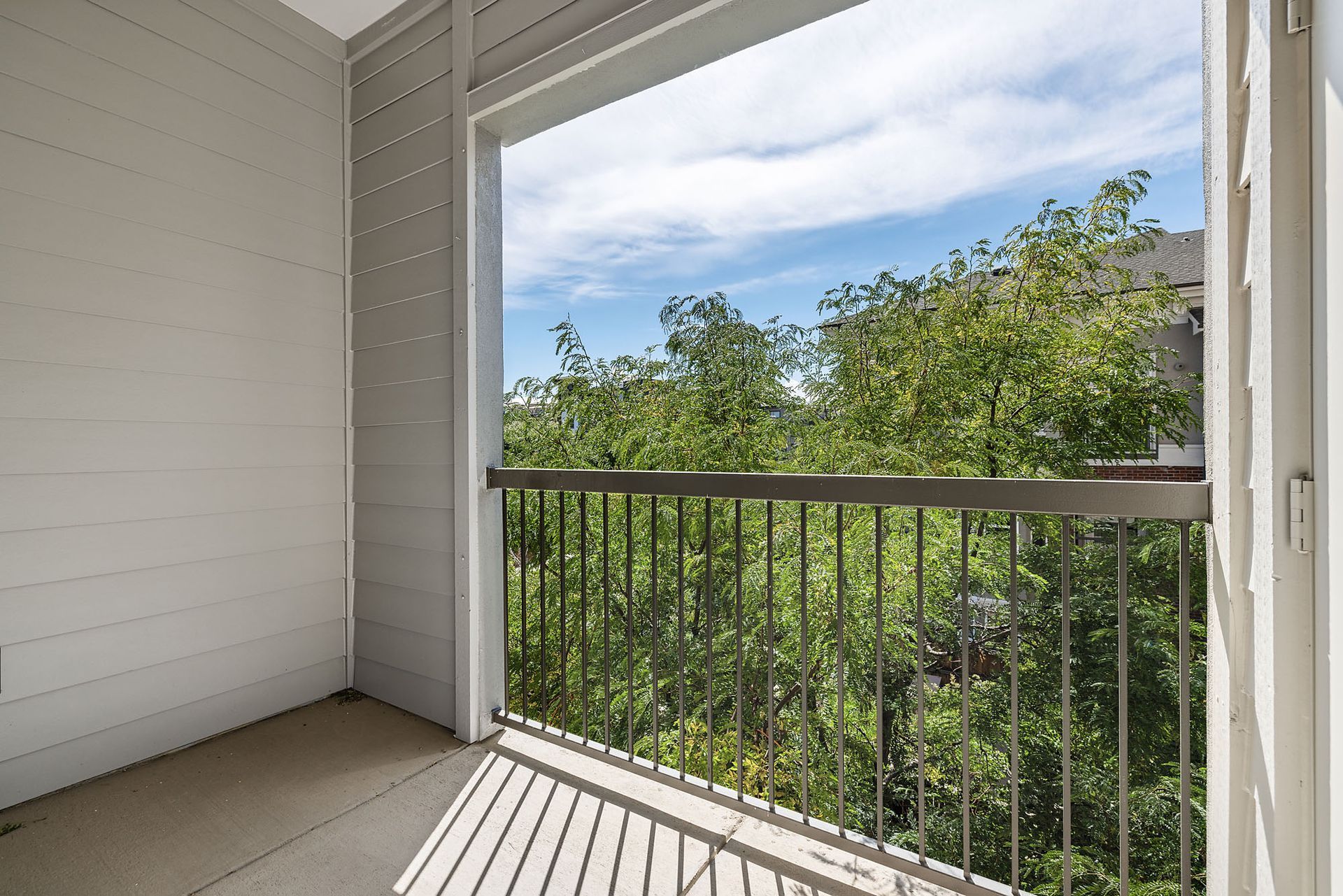 Covered balcony with white siding, black railing, and a view of green trees under a blue sky at The Marq at Ridgegate in Lone Tree, CO.