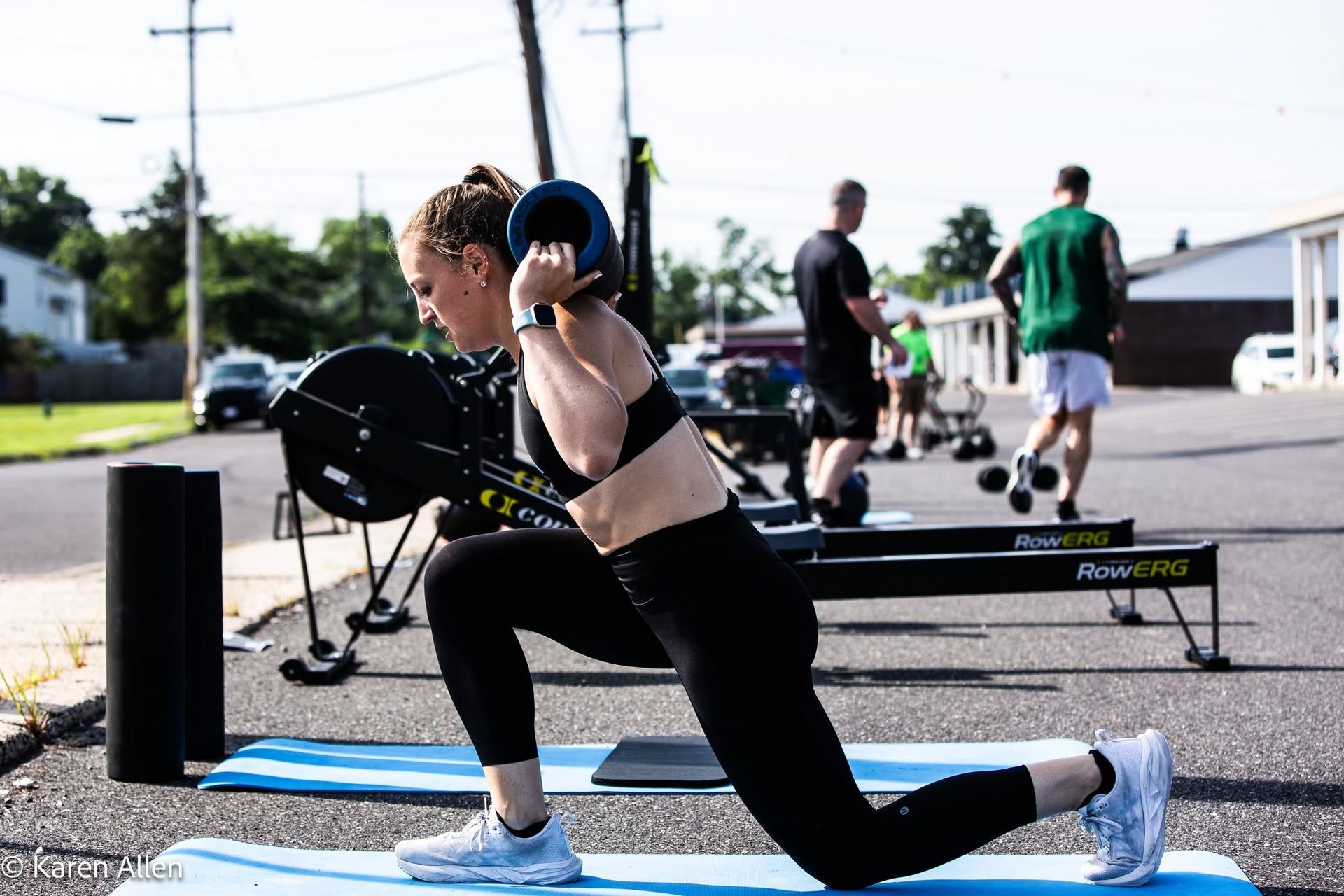 Woman doing a lunge with dumbbells on a mat outdoors during a workout class