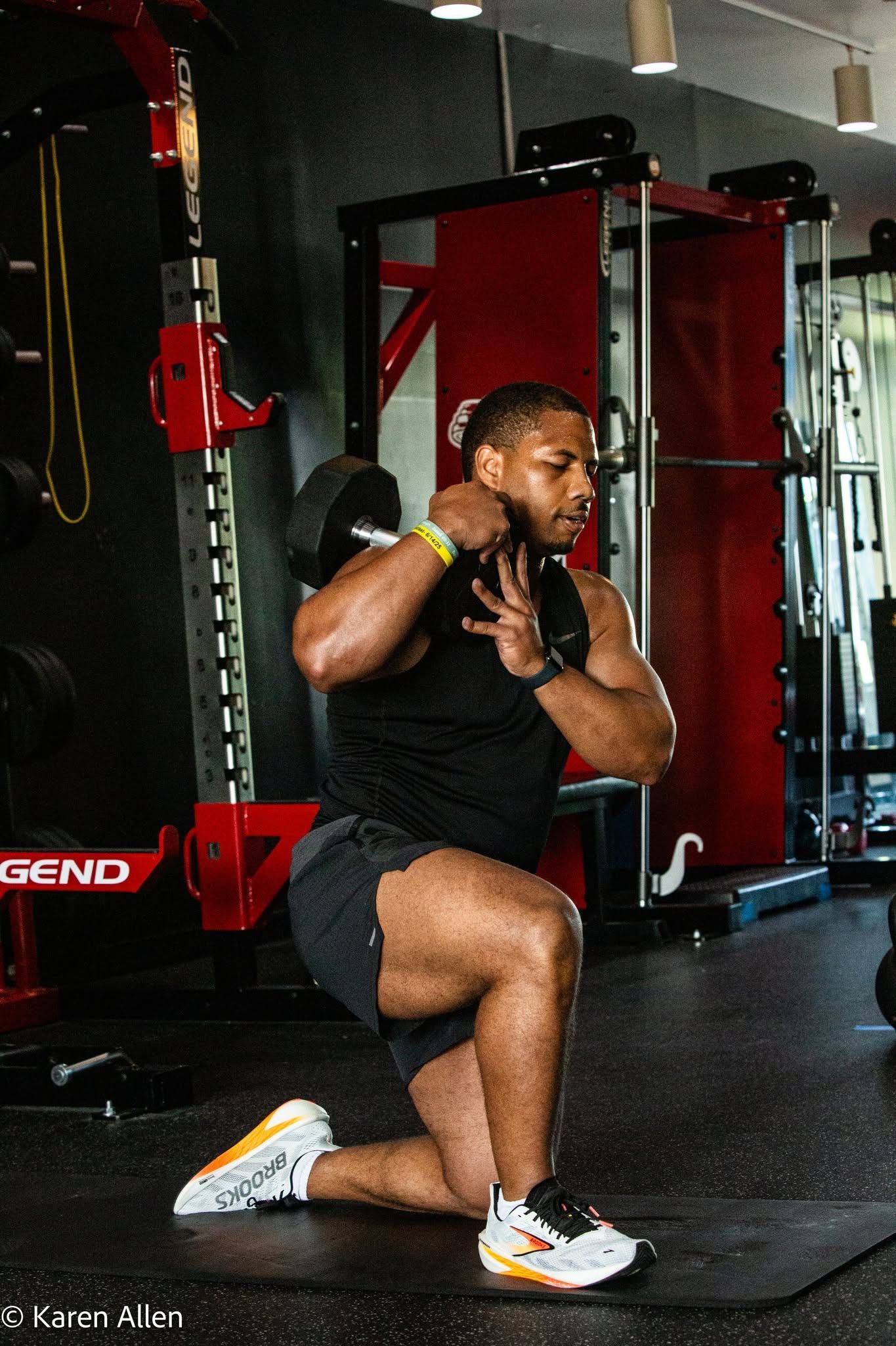 Man lunging in a gym, exercising beside red weight equipment and mirrors.