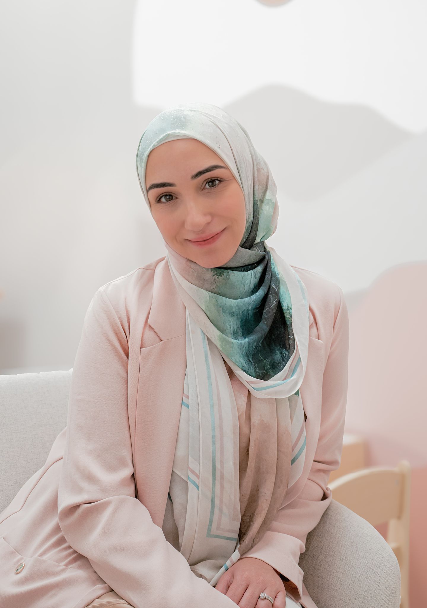 A woman wearing a hijab and a pink jacket is sitting on a couch.