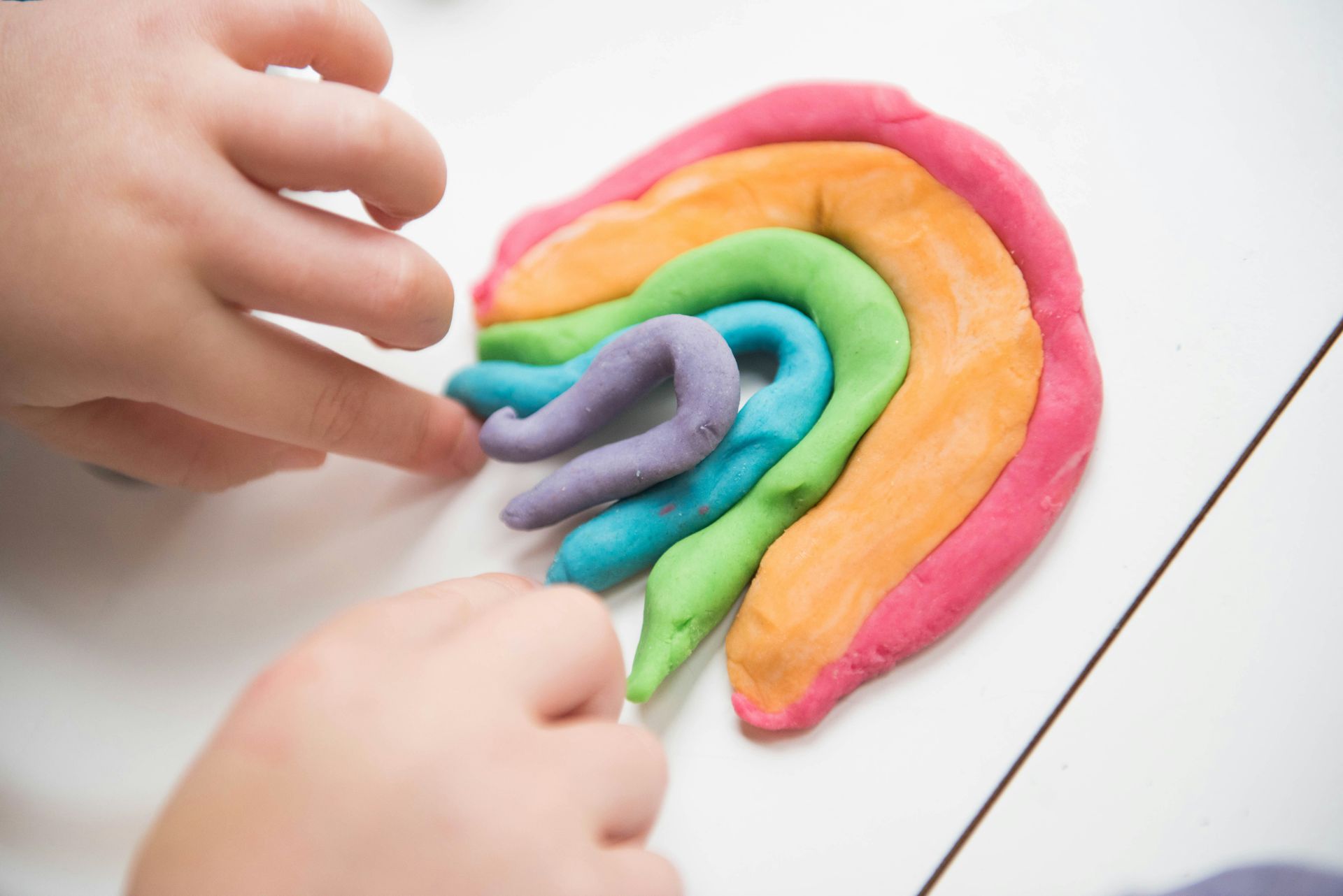 A child is playing with play dough and making a rainbow.