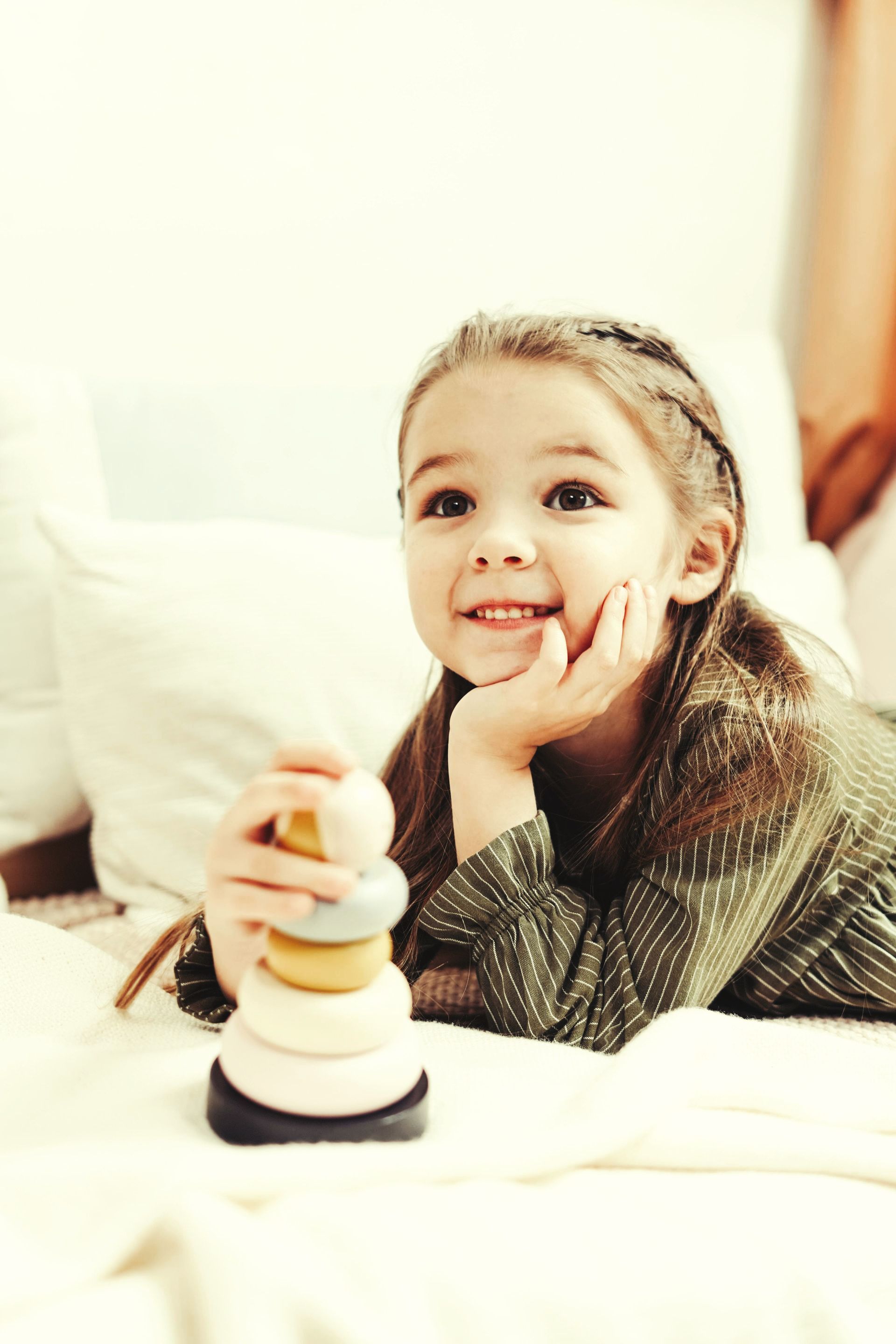 A little girl is laying on a bed holding a stacking toy.