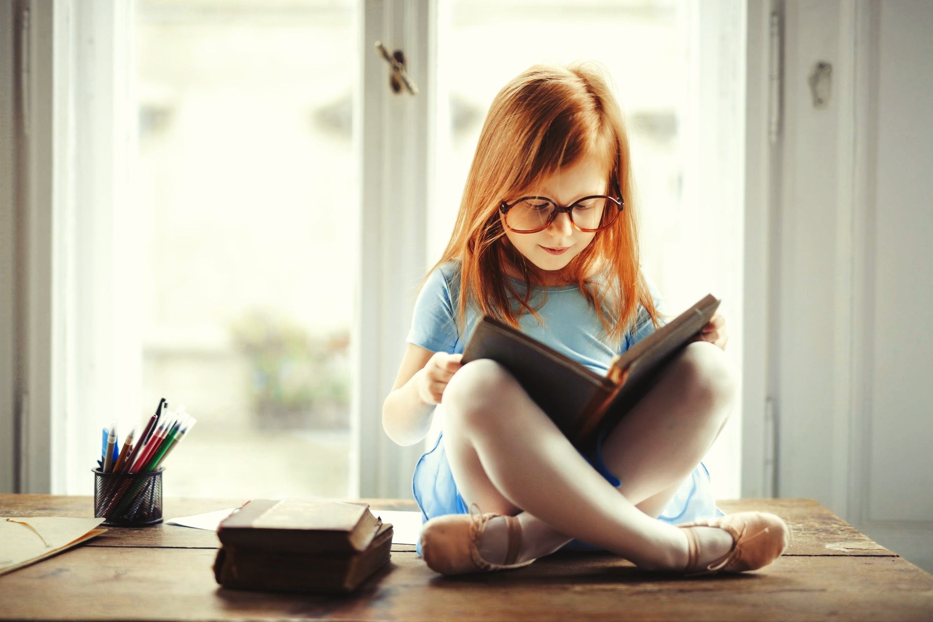 A little girl is sitting at a table reading a book.