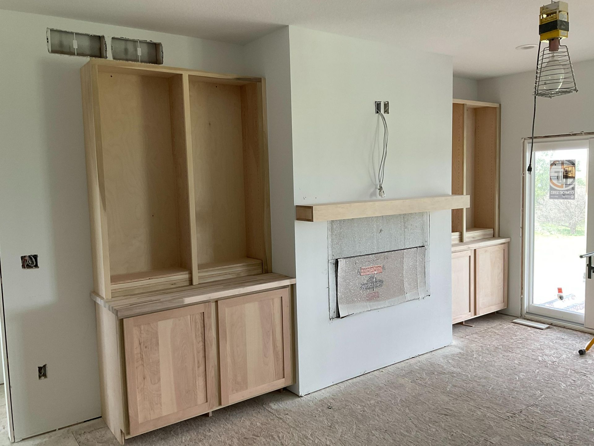 Unfinished room with built-in cabinets, white fireplace, and exposed light fixture near a doorway.