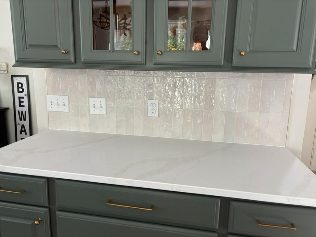 White kitchen countertop with gray cabinets, brass pulls, and a light backsplash under wall cabinets
