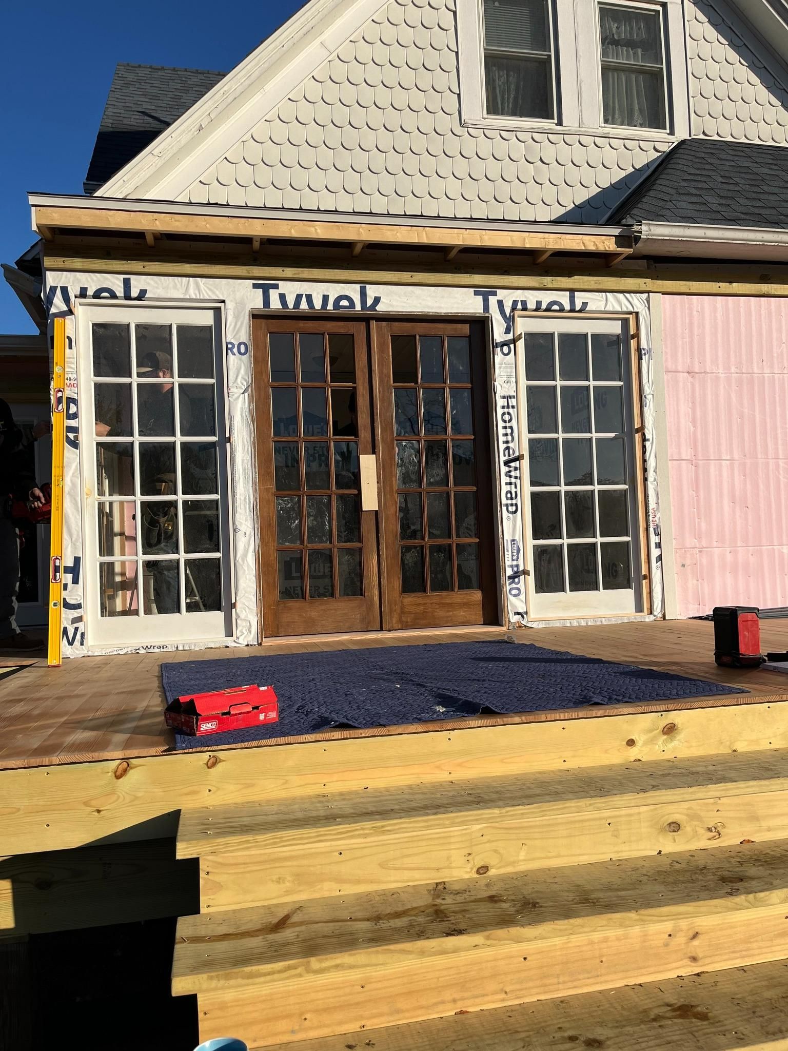 Storefront with glass double doors, white siding, and a wooden deck in front