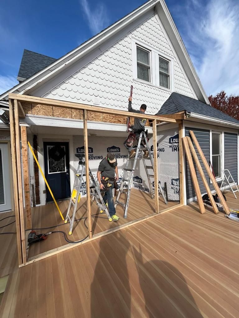 Person working on a house porch under construction with wooden framing and tools on a sunny day
