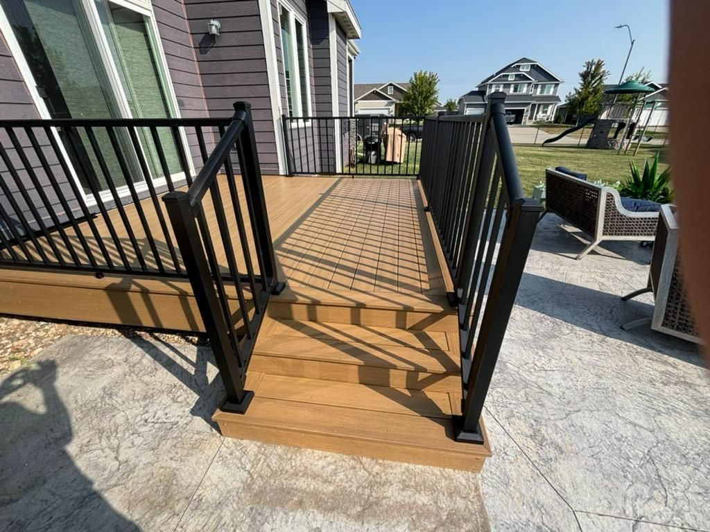 Wooden deck ramp with black railings leading to a house entrance on a sunny day
