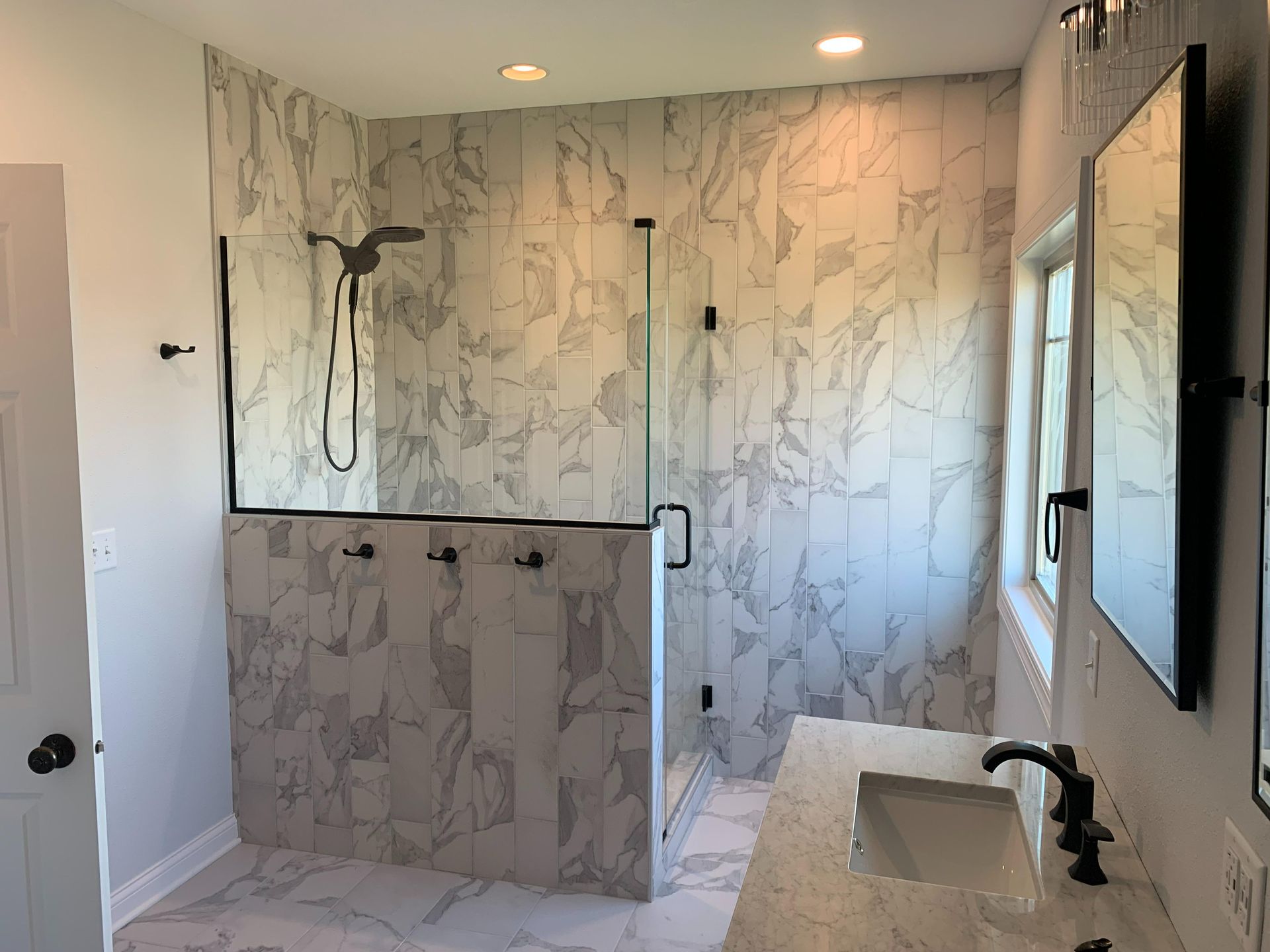 Modern bathroom with marble shower, glass partition, wall mirror, and double sink vanity.