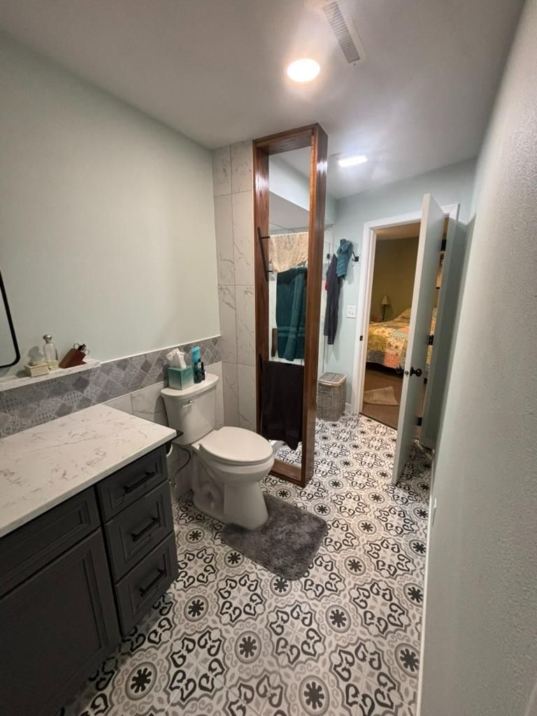 Modern bathroom with white toilet, dark vanity, marble countertop, patterned tile floor, and glass shower door