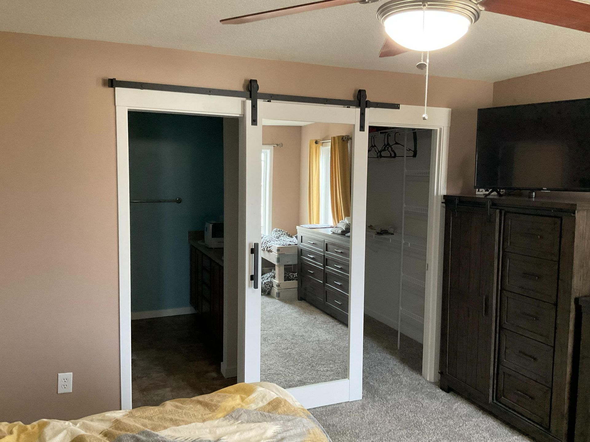 Bedroom with mirrored sliding closet doors, ceiling fan, TV, and dark wood dresser.