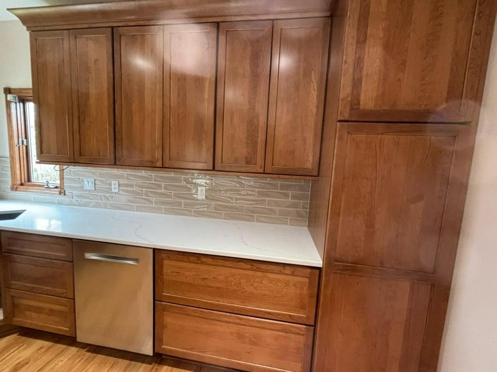 Wooden kitchen cabinets with white countertop, stone backsplash, and stainless dishwasher