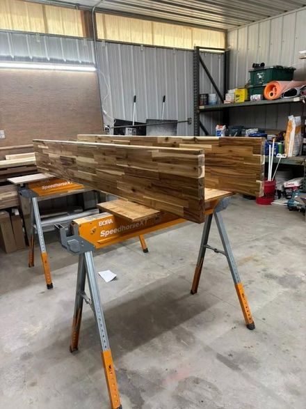 Stacked wooden boards on sawhorses in a workshop with tools and shelves in the background