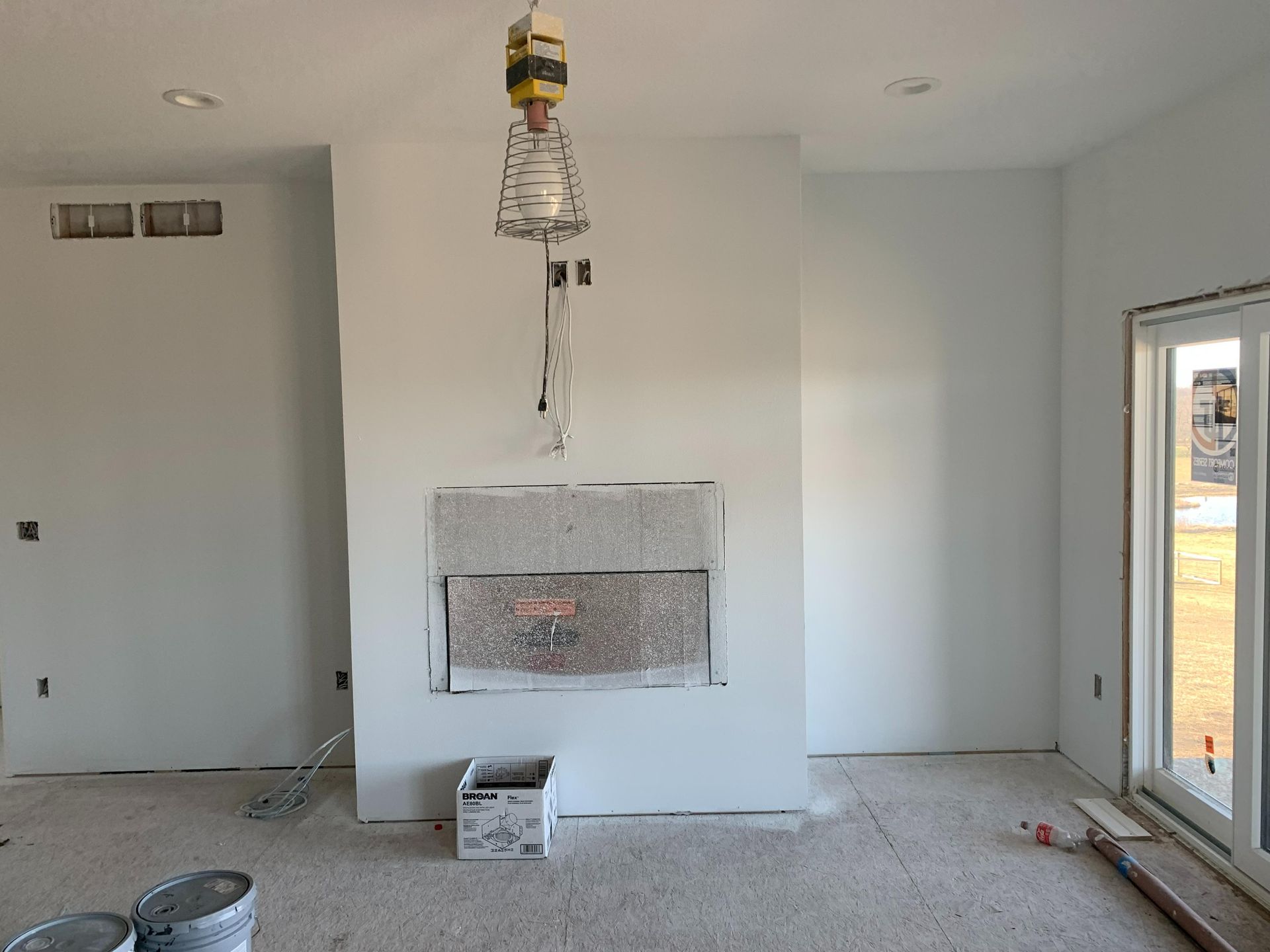 Unfinished living room with a fireplace, hanging light fixture, and open door to the outside.
