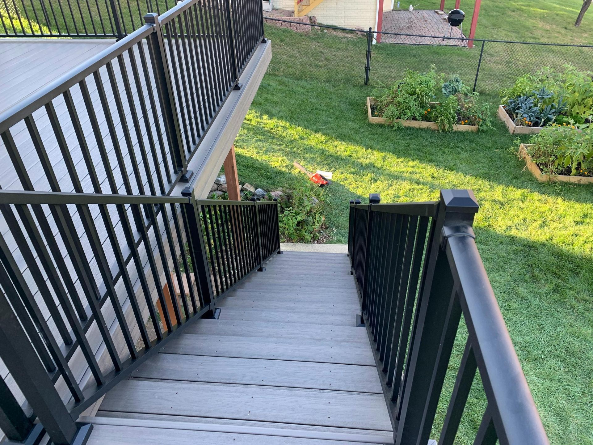 Outdoor stairs with black railings leading down to a grassy yard and garden beds.