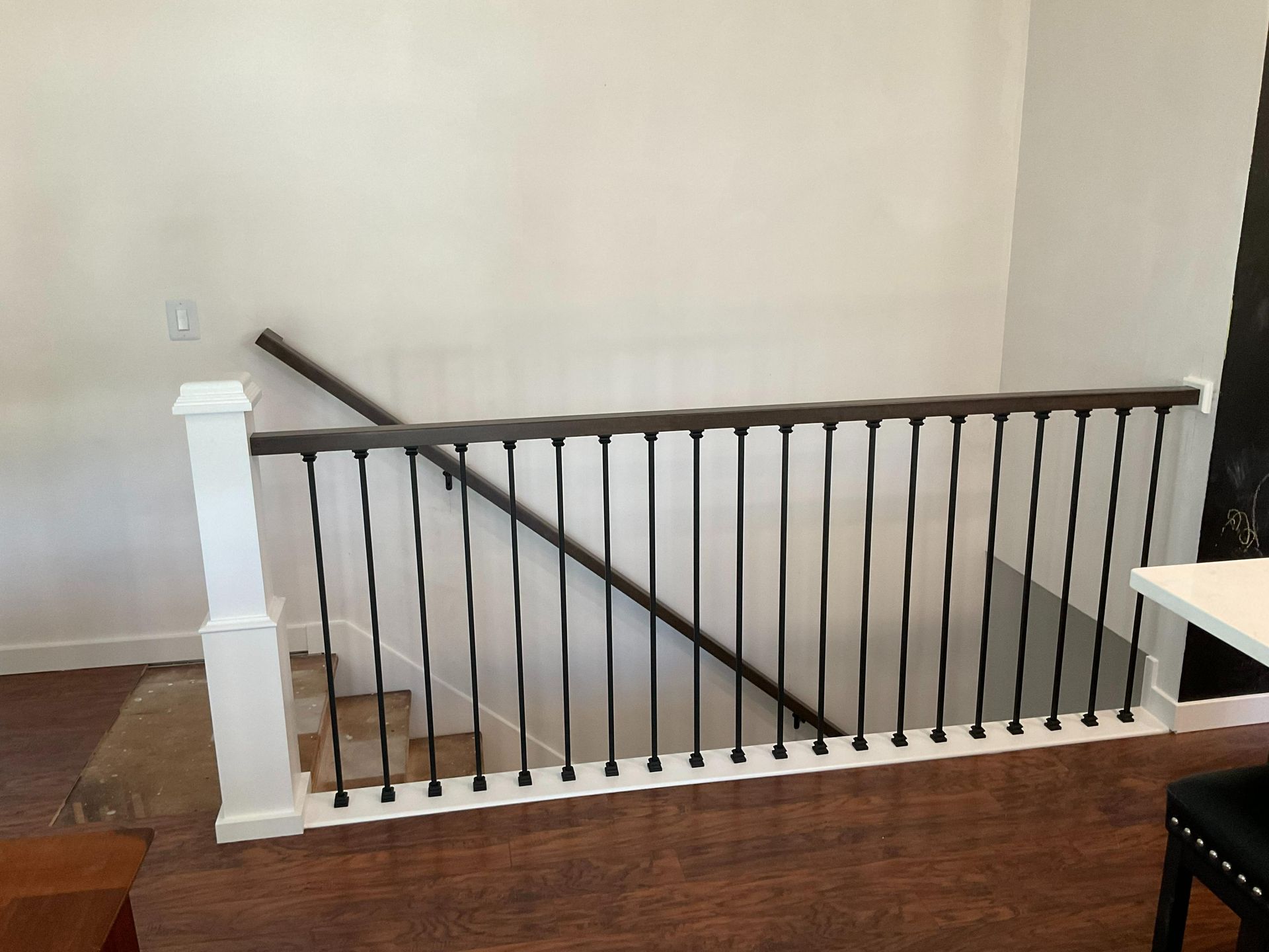 Indoor staircase with black balusters and white posts, viewed from a hallway with wood flooring.