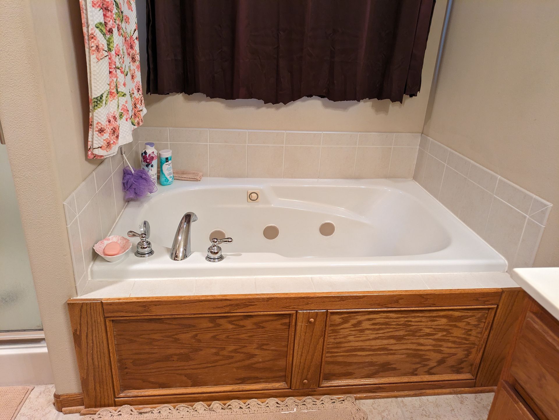 Bathroom bathtub with beige tile surround, wooden cabinet front, and dark curtain above the tub.