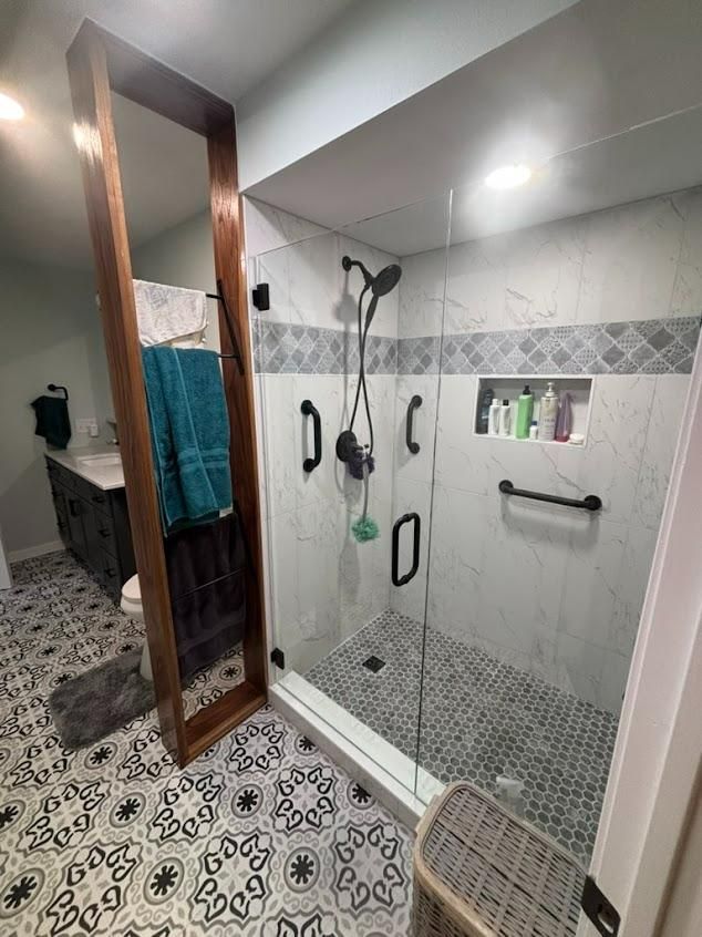 Modern tiled bathroom with a glass shower, patterned floor, and hanging towels