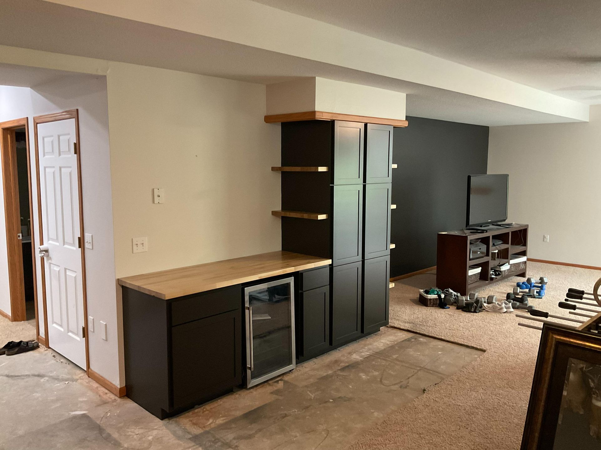 Unfinished room with black cabinets, wood countertop, and a TV on a stand against a dark wall.