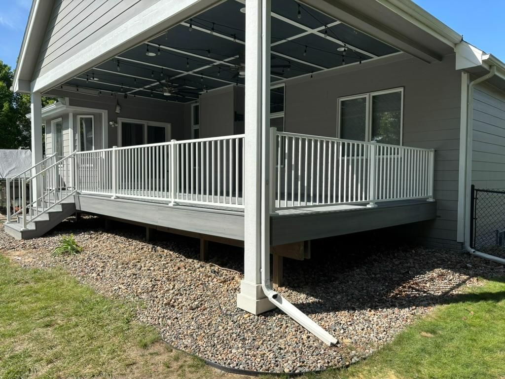 Covered porch with white railing and steps on a gray house, set over a gravel foundation